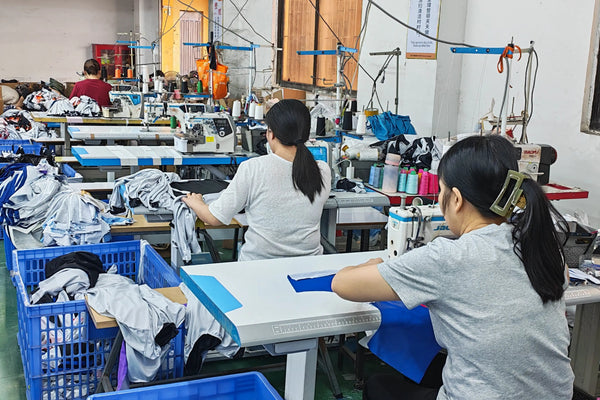 Workers operating industrial sewing machines to stitch custom sportswear panels together in the factory.