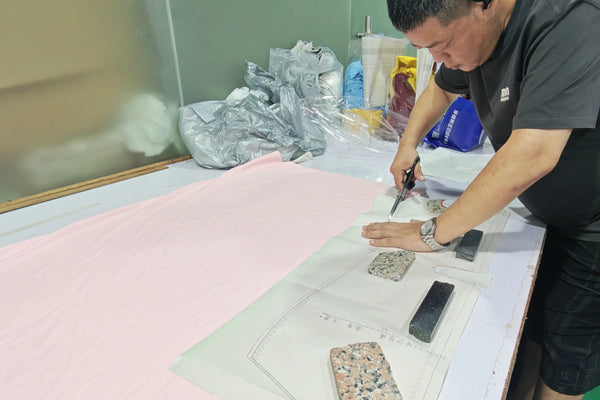 Worker carefully cutting pink fabric using a paper pattern and scissors in the sportswear manufacturing workshop.