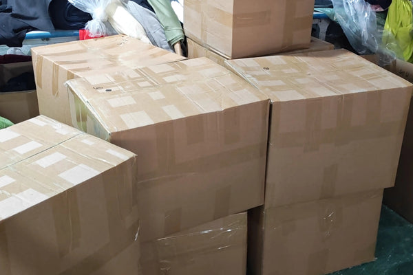 Stacked cardboard boxes containing finished custom sportswear orders ready for international shipping.